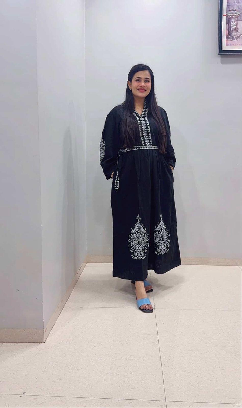 Woman wearing a black outfit with white embroidery in an indoor setting