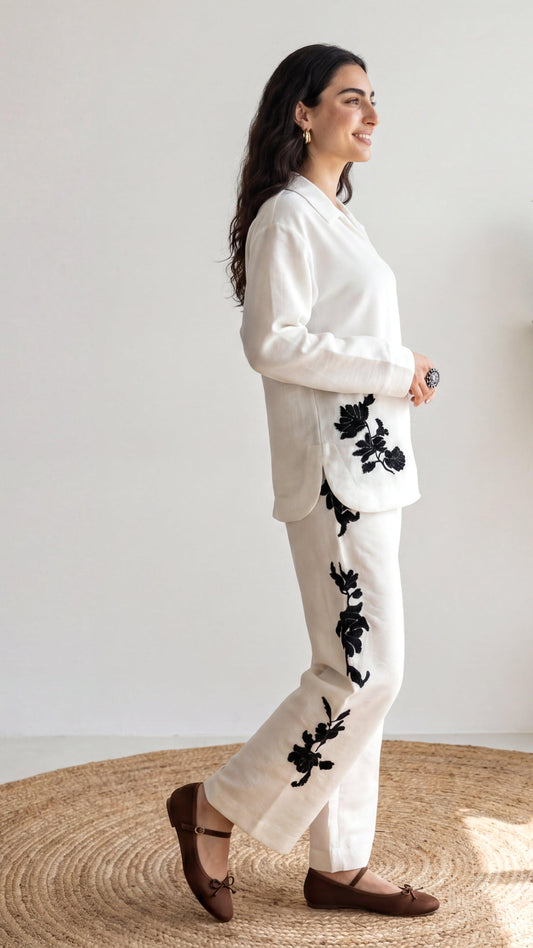 Woman wearing a white outfit with black floral patterns on a neutral background