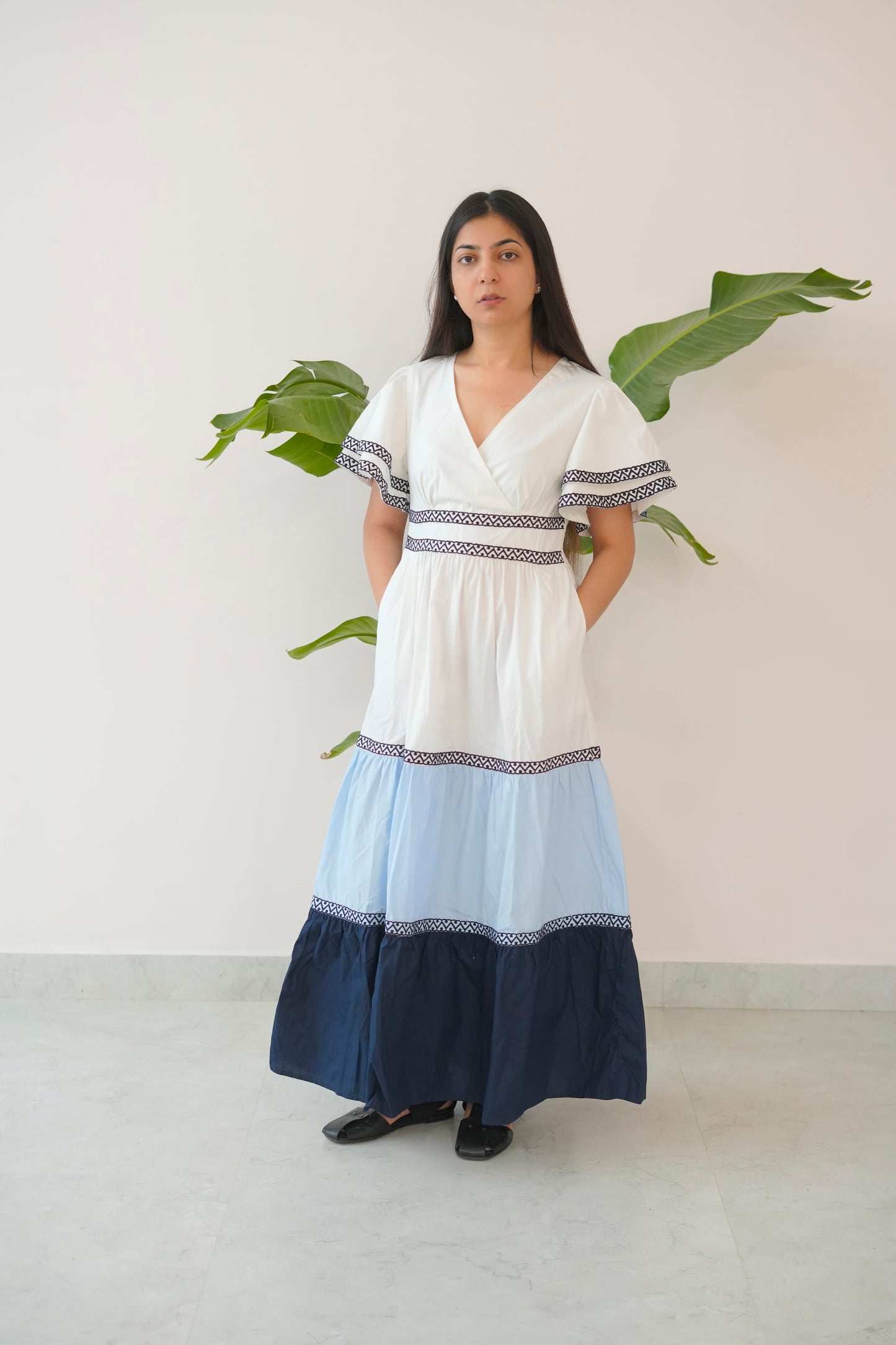 Woman wearing a white dress with blue accents standing against a plain background