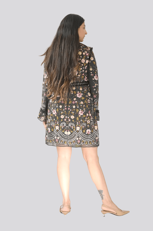Woman wearing a floral dress standing in front of a plant against a white wall