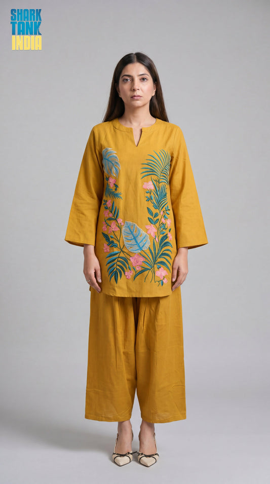 Woman wearing a mustard yellow outfit with floral embroidery on a gray background