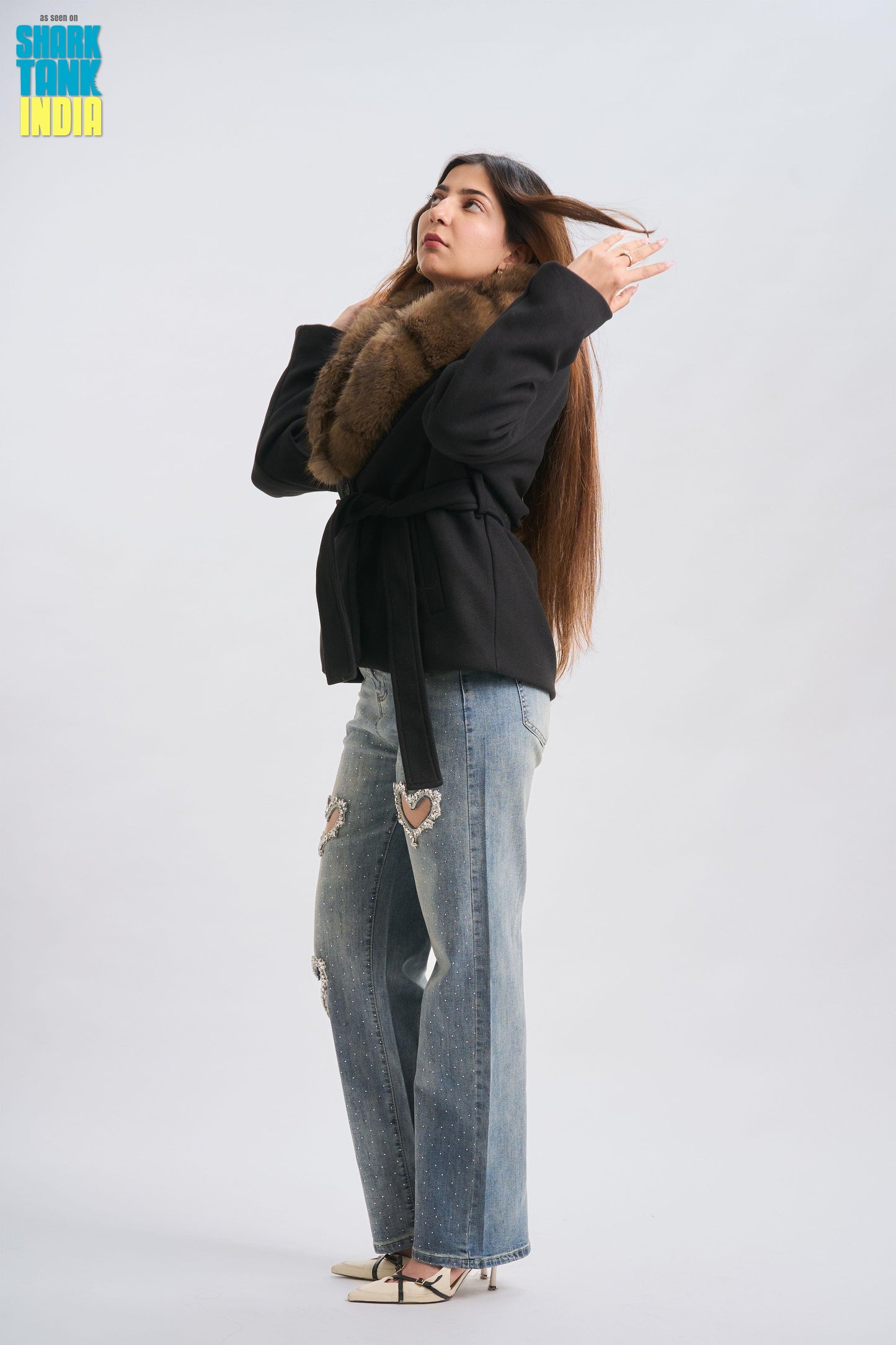 Woman wearing a black coat with fur trim and ripped jeans on a white background