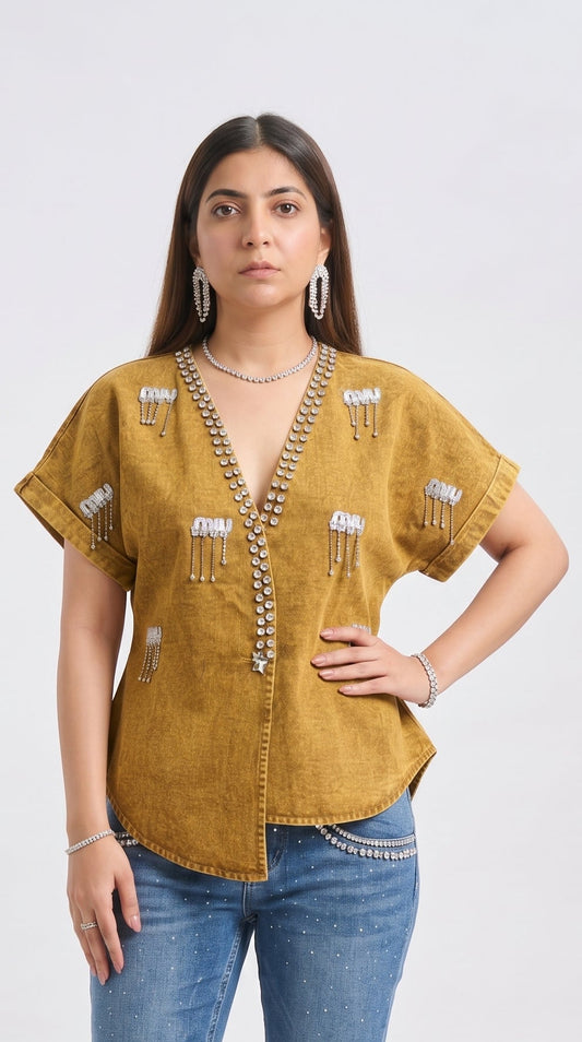 Woman wearing a mustard yellow top with embellishments and blue jeans on a white background