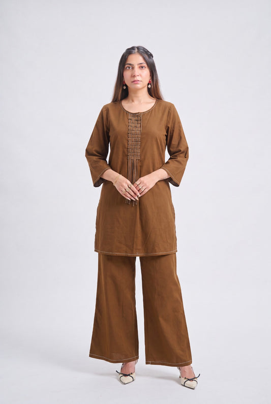 A woman modeling a brown two-piece kurta and trouser set against a plain light gray studio background.