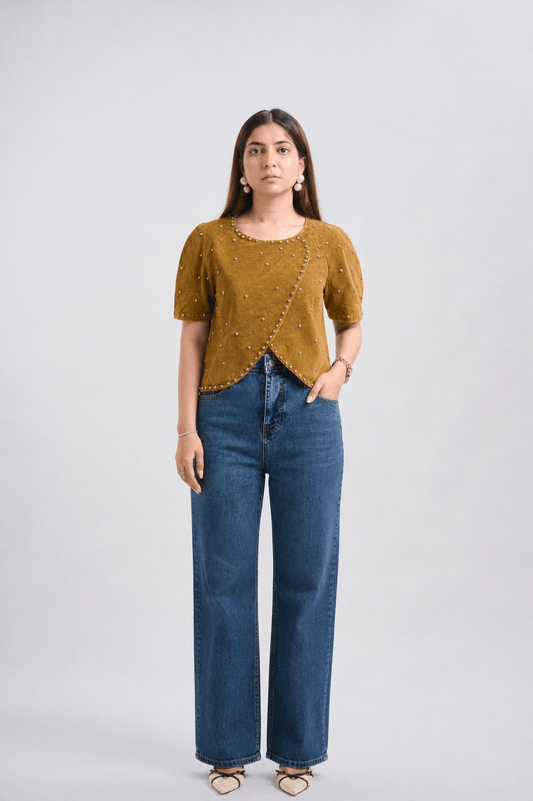 Woman wearing a mustard yellow top and blue jeans on a white background