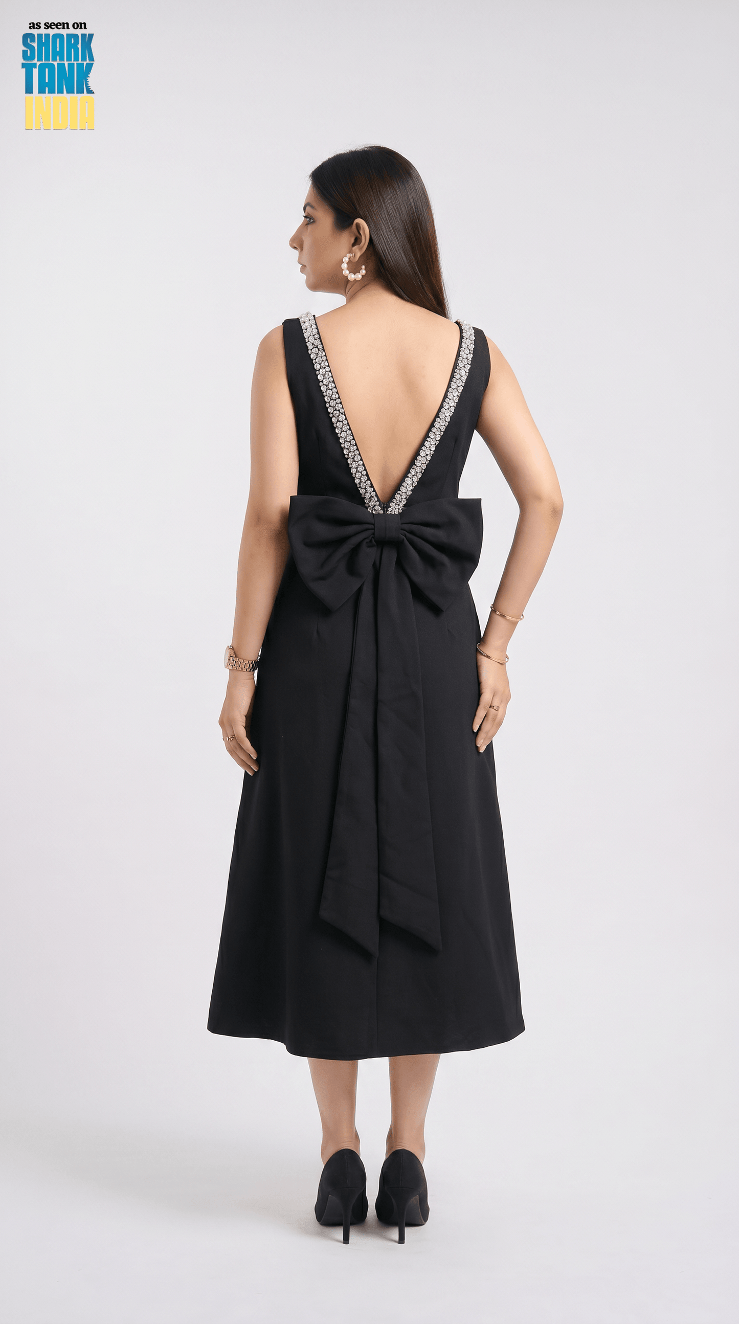Black dress with a large bow detail on the back, worn by a model against a white background.