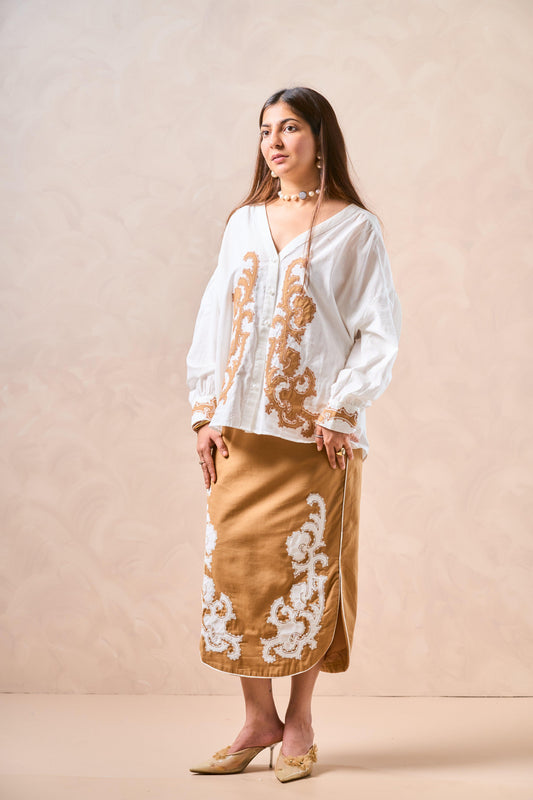 Woman wearing a white embroidered blouse and tan skirt against a beige background