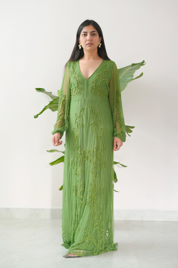 Woman wearing a green embroidered dress with leaf-like accessories on a white background