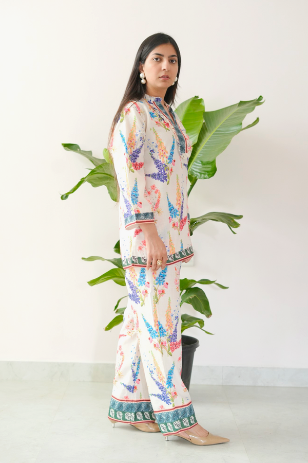 Woman wearing a colorful patterned outfit standing next to a potted plant.