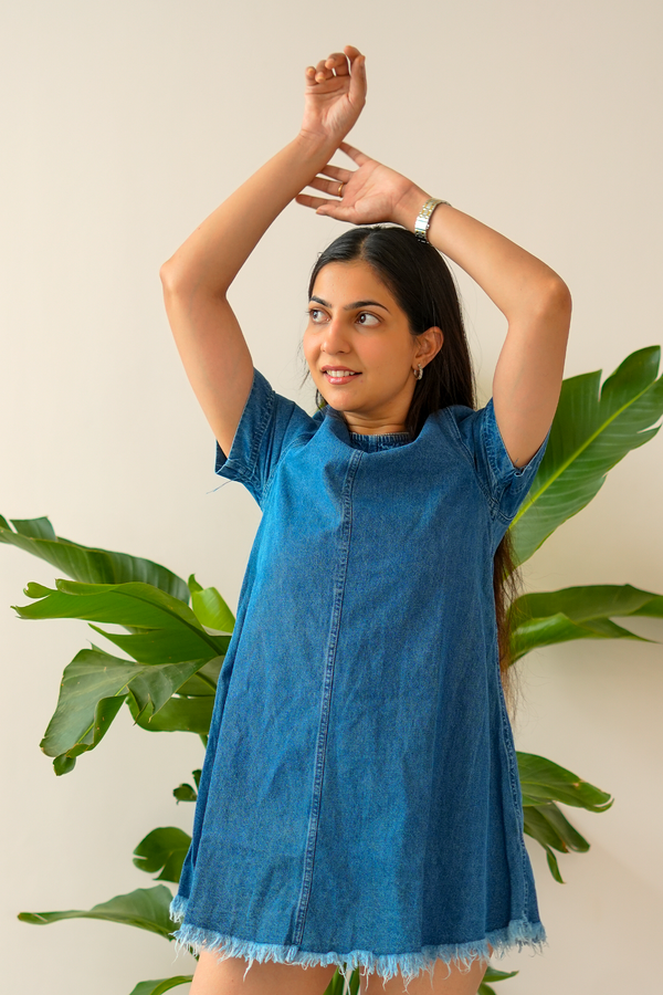 Woman wearing a blue denim dress with green plants in the background