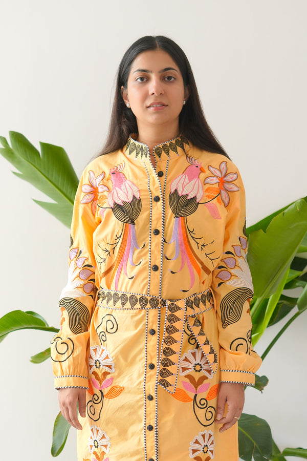 Woman wearing a bright yellow embroidered outfit with green plants in the background