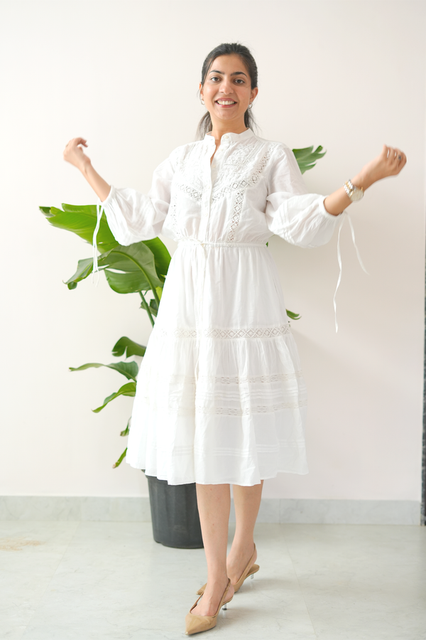Woman wearing a white dress standing in a room with a plant in the background