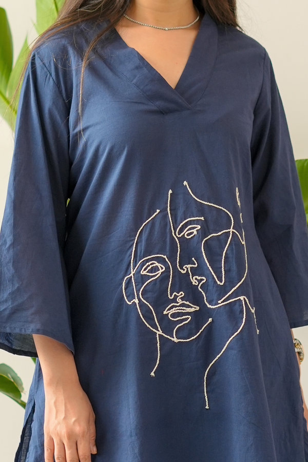 Navy blue dress with abstract face design worn by a person, against a neutral background.