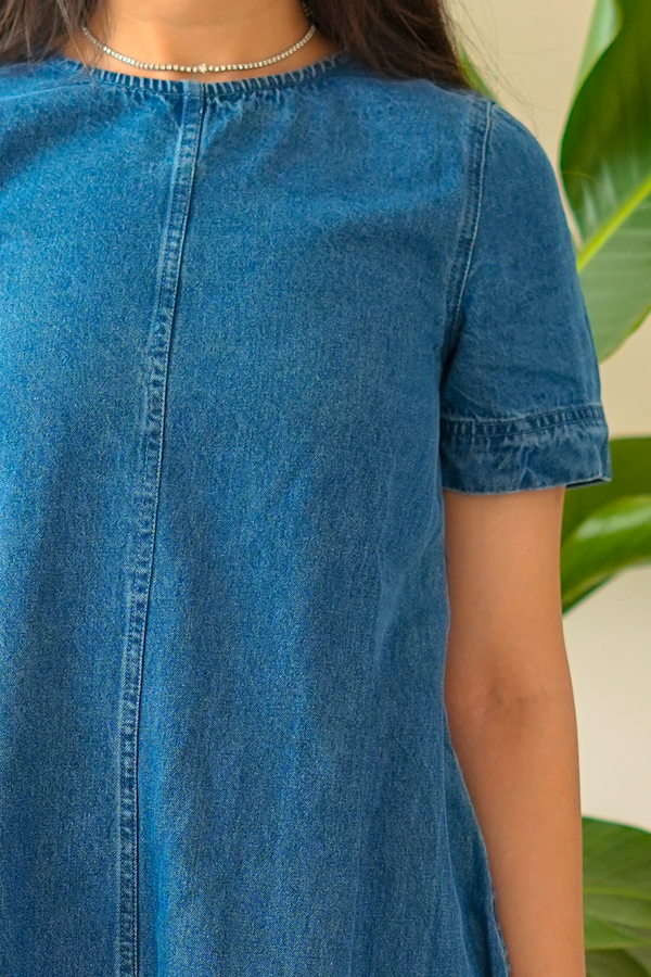 Person wearing a blue denim dress with a blurred background