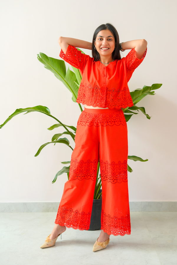 Woman wearing a bright red outfit with lace details in front of a plant