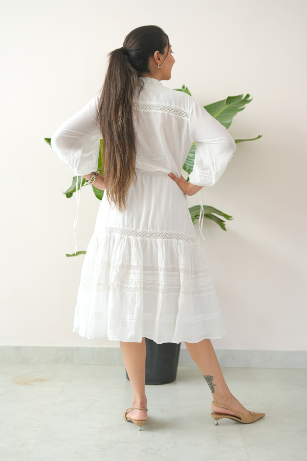 Woman wearing a white dress with lace details, standing against a plain background.