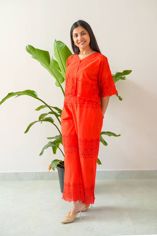 Woman wearing a bright red outfit with lace details standing next to a plant indoors.