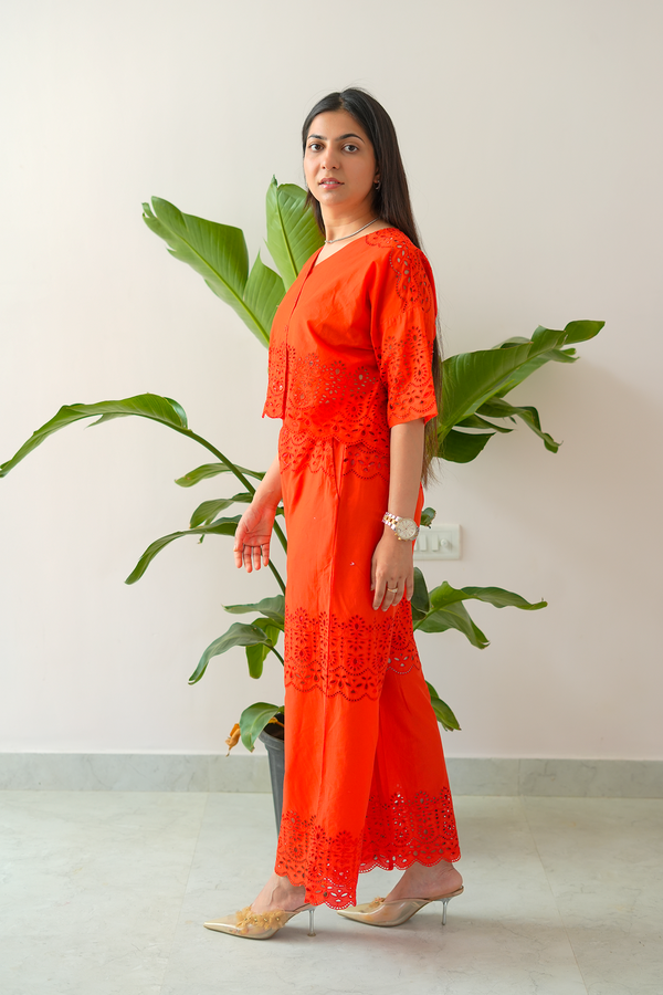 Woman in an orange outfit standing next to a plant indoors
