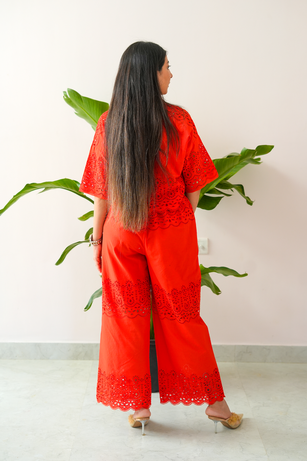 Woman wearing a red embroidered outfit standing in front of a white wall with a plant.