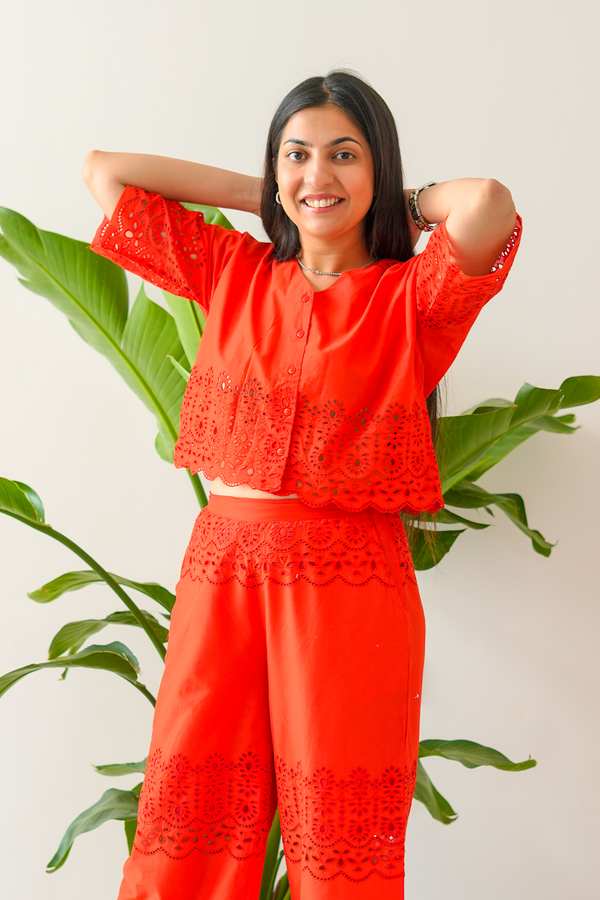 Woman wearing a red outfit with lace details in front of green plants.