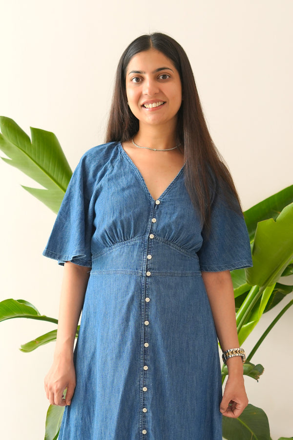 Woman wearing a blue dress standing in front of green plants
