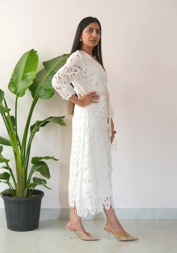 Woman in a white lace dress standing next to a potted plant.