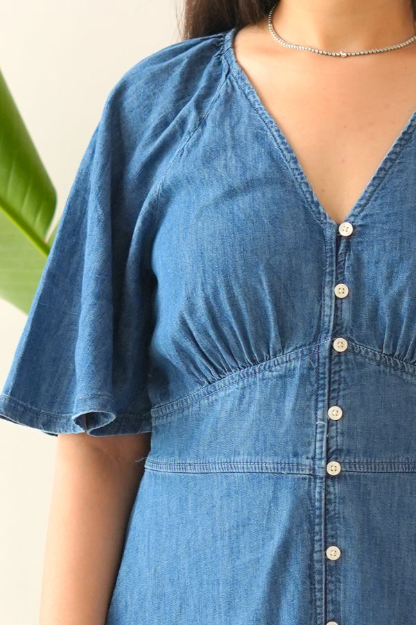 Blue denim dress with button details on a neutral background