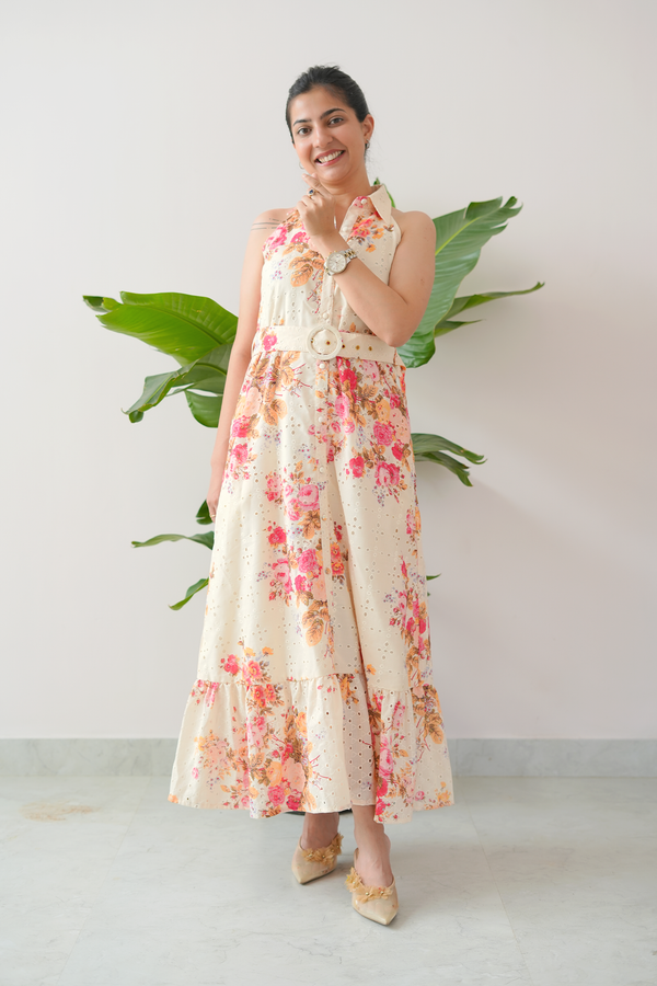 Woman wearing a floral dress standing against a white wall with a plant.