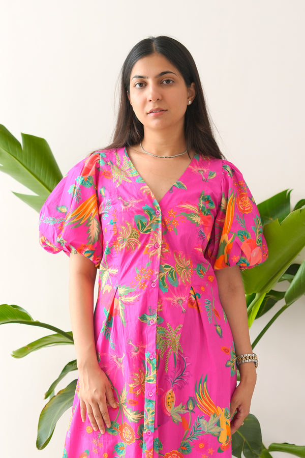 Woman wearing a bright pink dress with colorful floral patterns against a white background