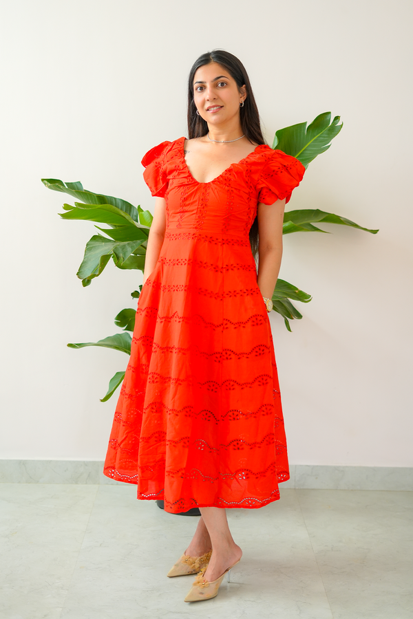 Woman wearing a red dress with ruffled sleeves against a white wall with green plants.