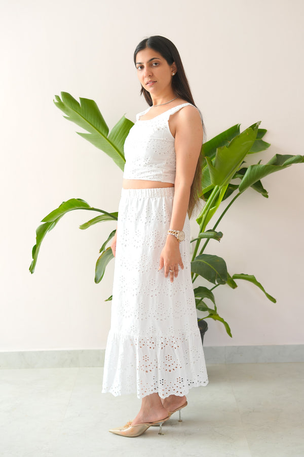 Woman in a white outfit standing next to a plant against a light background