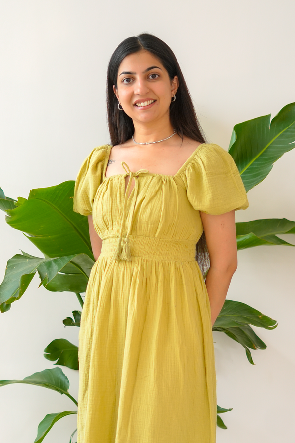 Woman in a yellow dress standing in front of green plants against a white wall