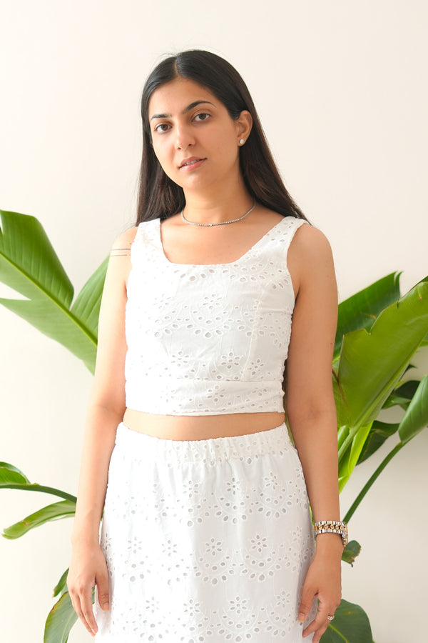 Woman wearing a white sleeveless top and skirt with green plants in the background