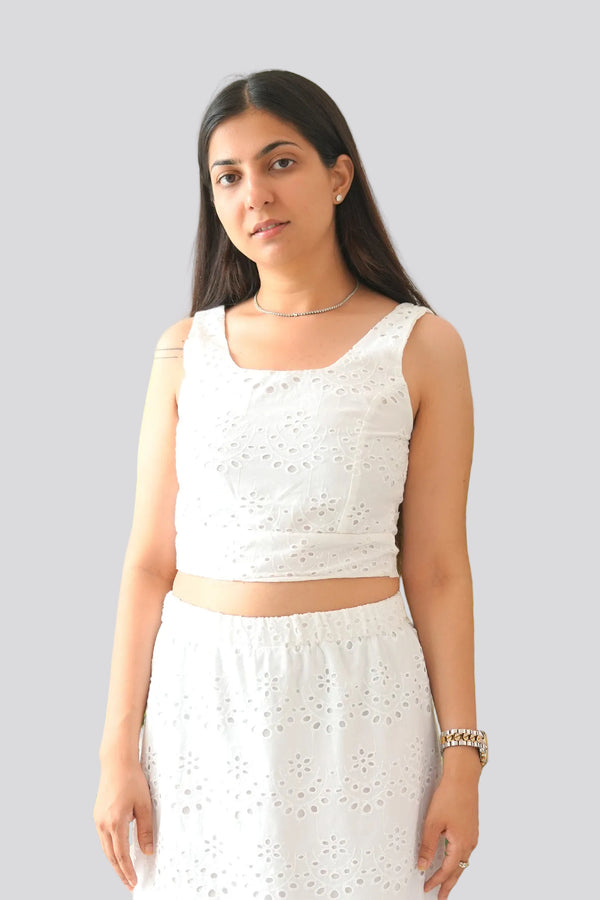 Woman wearing a white sleeveless top and skirt with green plants in the background