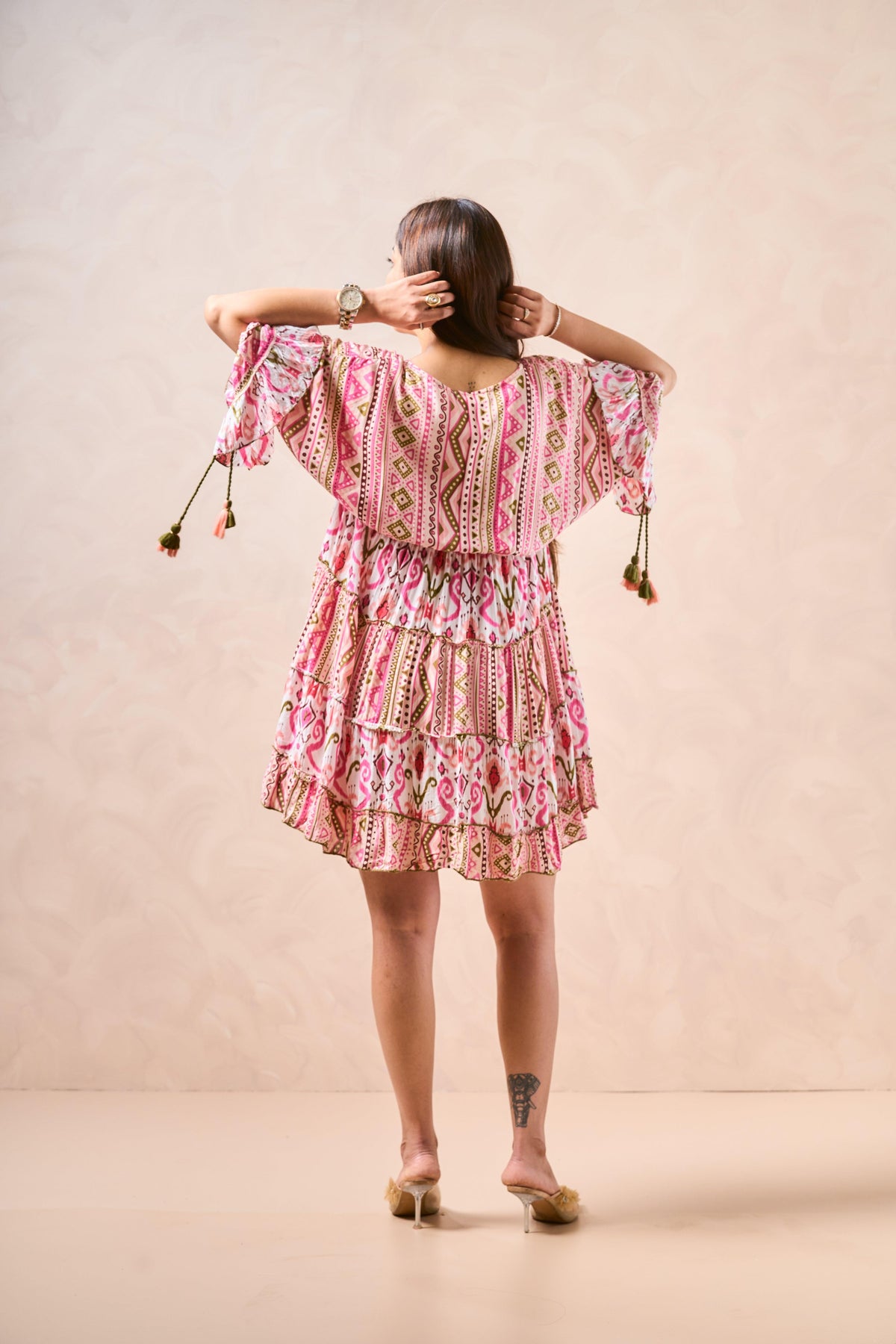 Woman wearing a pink patterned dress with tassels on a beige background