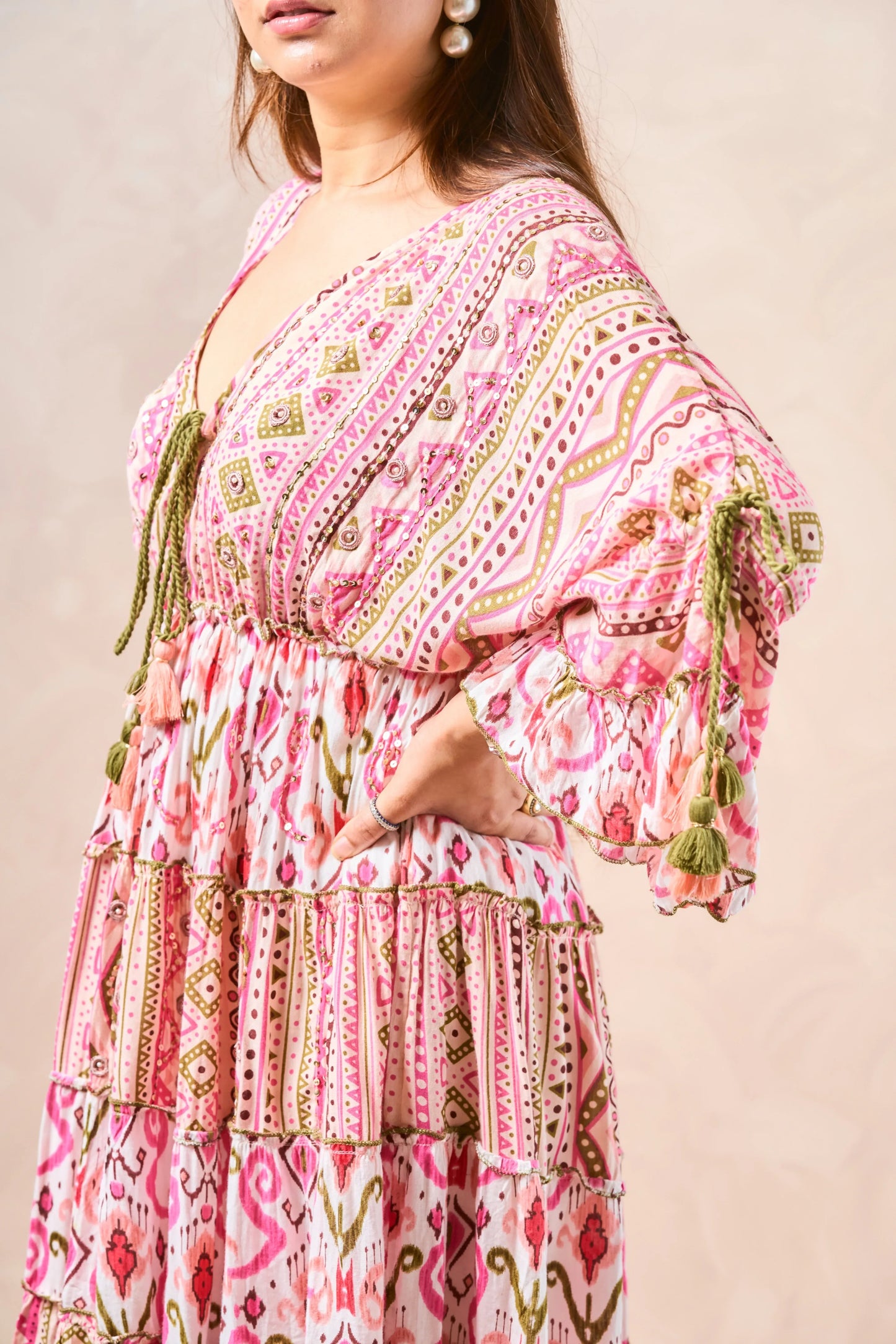 Woman wearing a pink patterned dress with tassels on a beige background