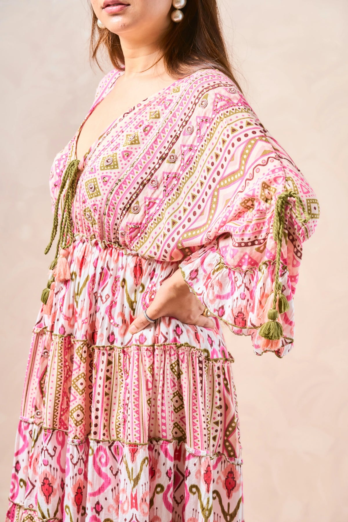 Woman wearing a pink patterned dress with tassels on a beige background