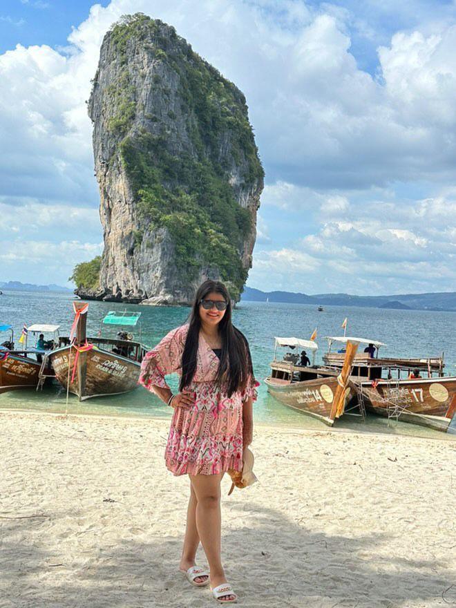 Woman in a pink dress standing on a beach with limestone karst towers and boats in the background.