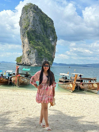 Woman in a pink dress standing on a beach with limestone karst towers and boats in the background.