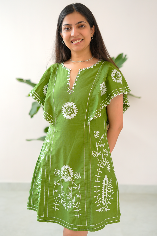 Woman wearing a green dress with white floral embroidery against a white background