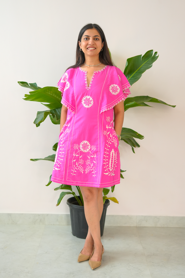Woman wearing a pink dress with white floral patterns standing in front of a plant.