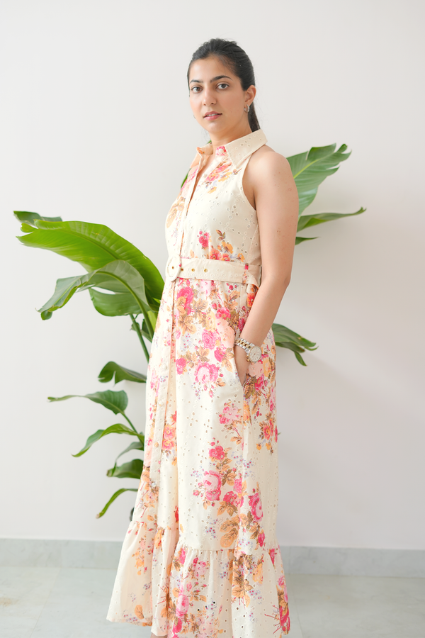 Woman wearing a floral dress standing next to a plant against a white wall