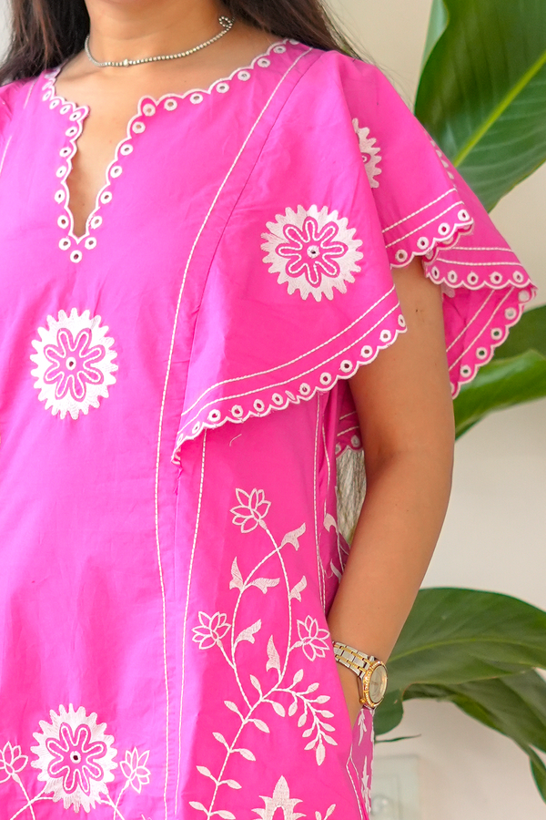 Person wearing a bright pink outfit with white floral patterns, standing against a neutral background.