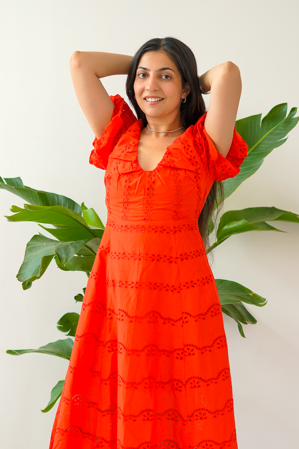 Woman wearing a red dress standing against a white wall with green plants.