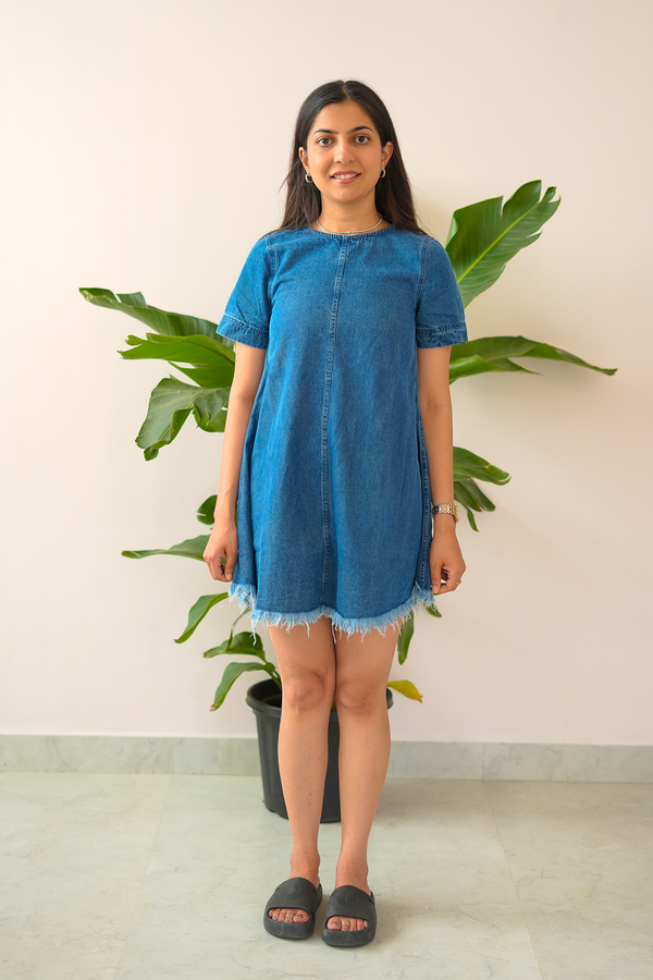 Woman wearing a blue dress standing in front of a plant against a white wall
