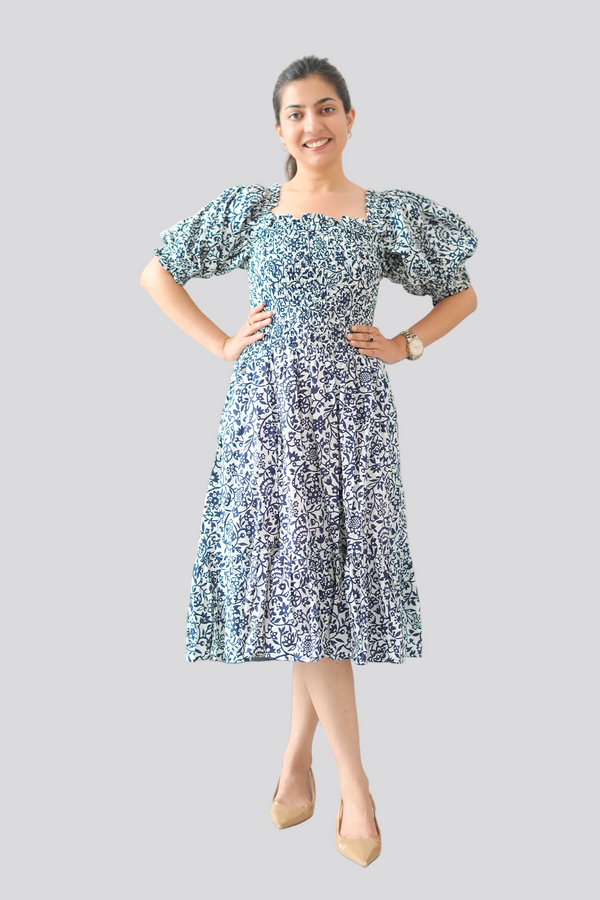 Woman wearing a blue floral dress standing next to a plant indoors.