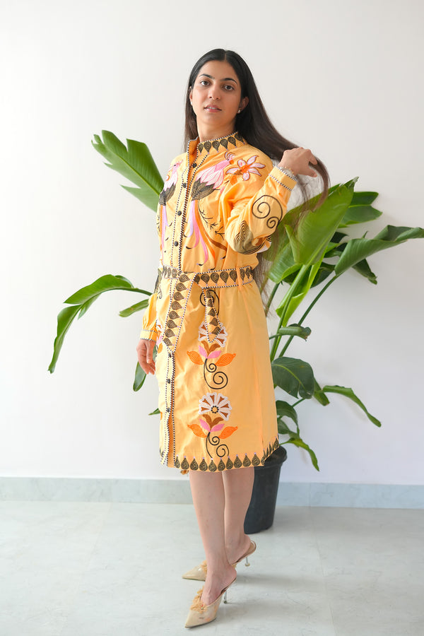 Woman wearing a yellow embroidered dress standing in front of a plant