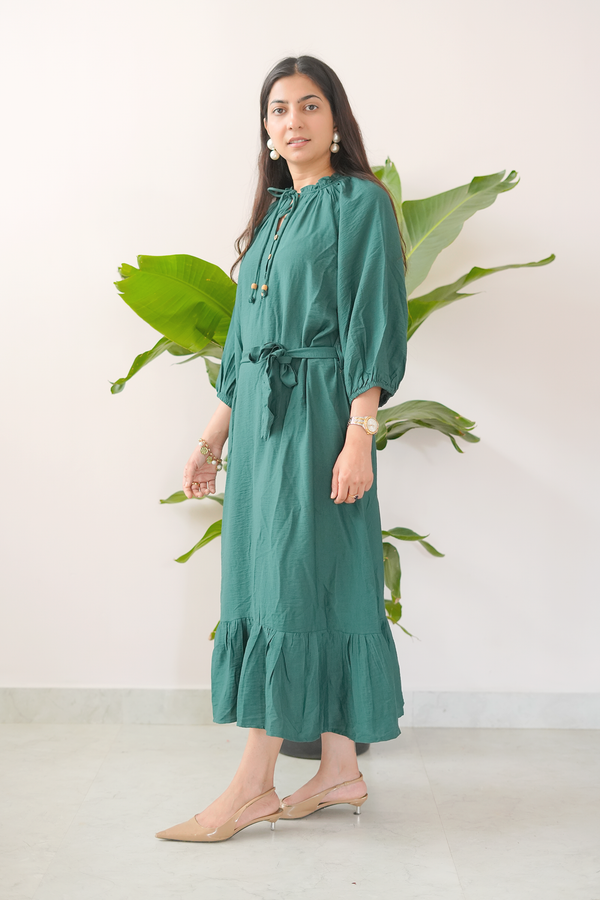 Woman wearing a green dress standing in front of a white wall with a plant.