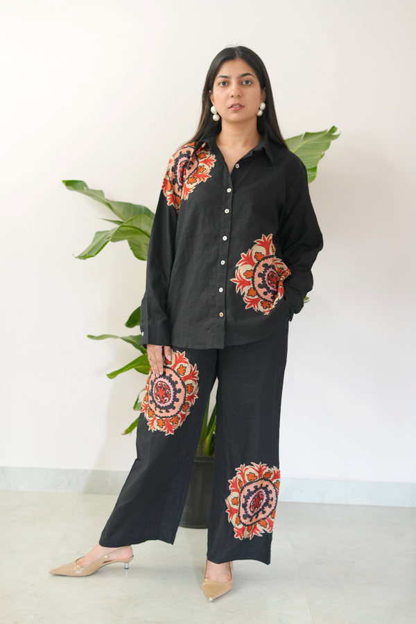 Woman wearing a black outfit with colorful floral patterns standing against a white background.