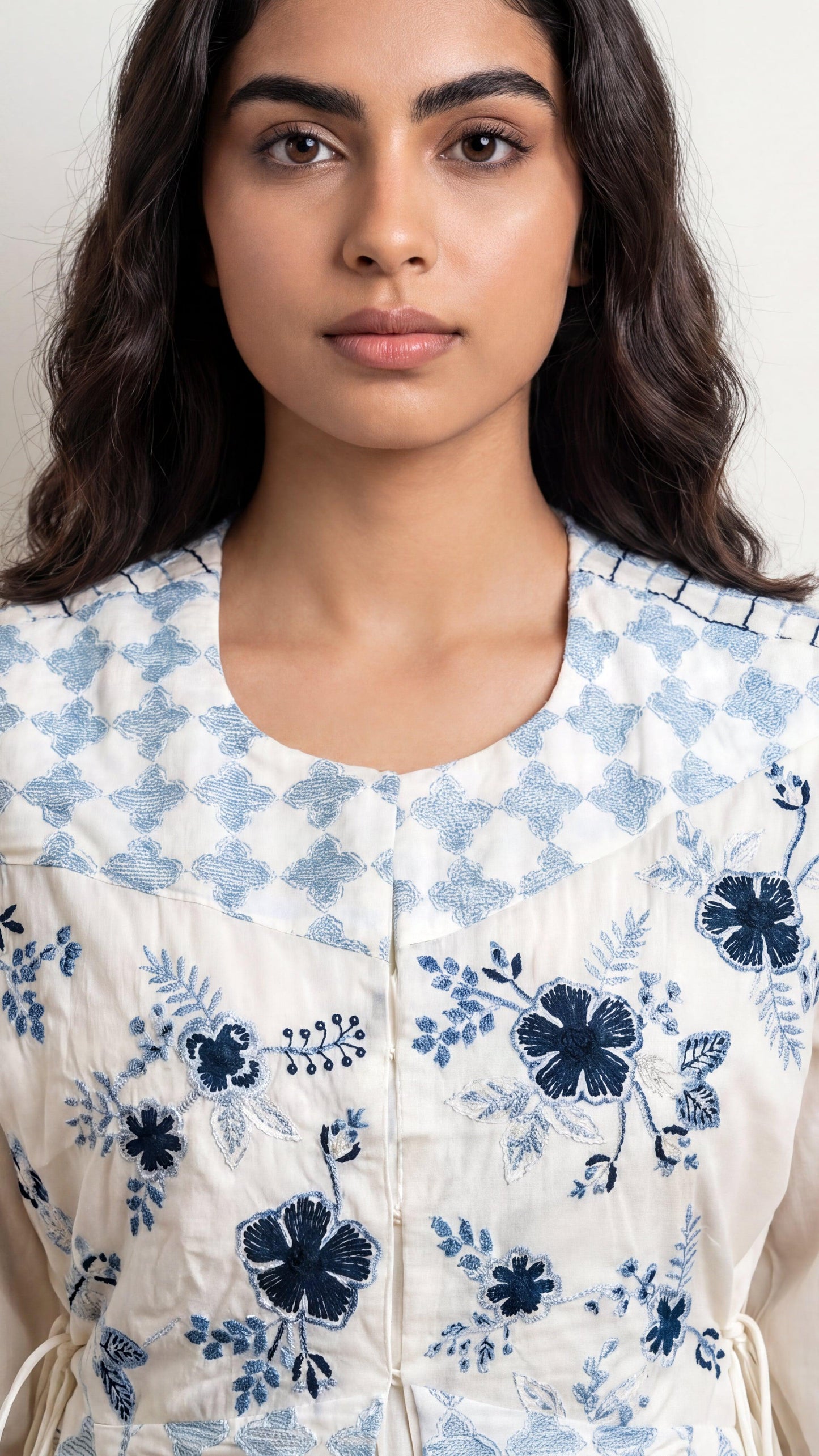 Woman wearing a white floral jacket with blue flowers on a plain background